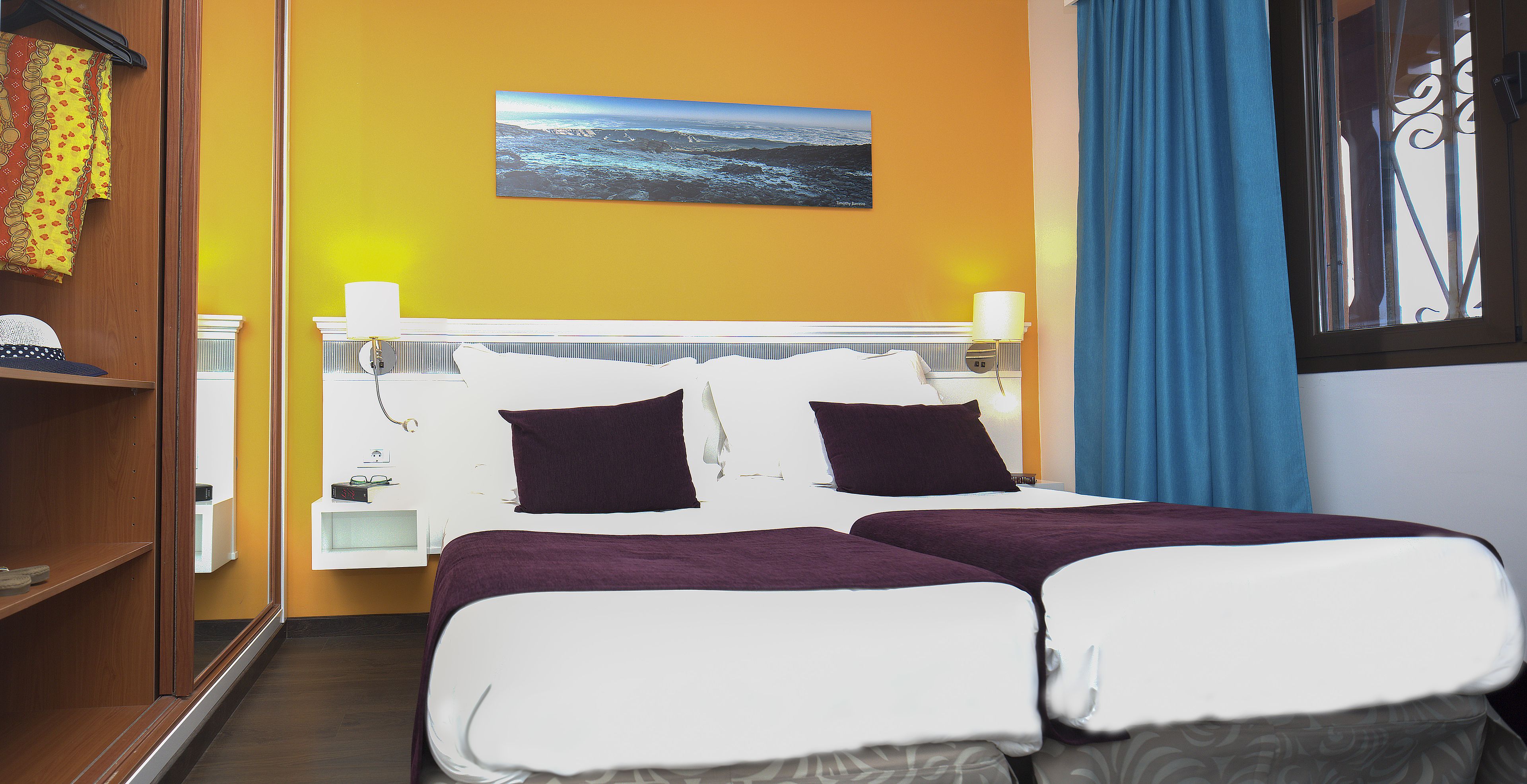 Een hotelkamer met een bed, nachtkastje, lamp en een schilderij aan de muur.