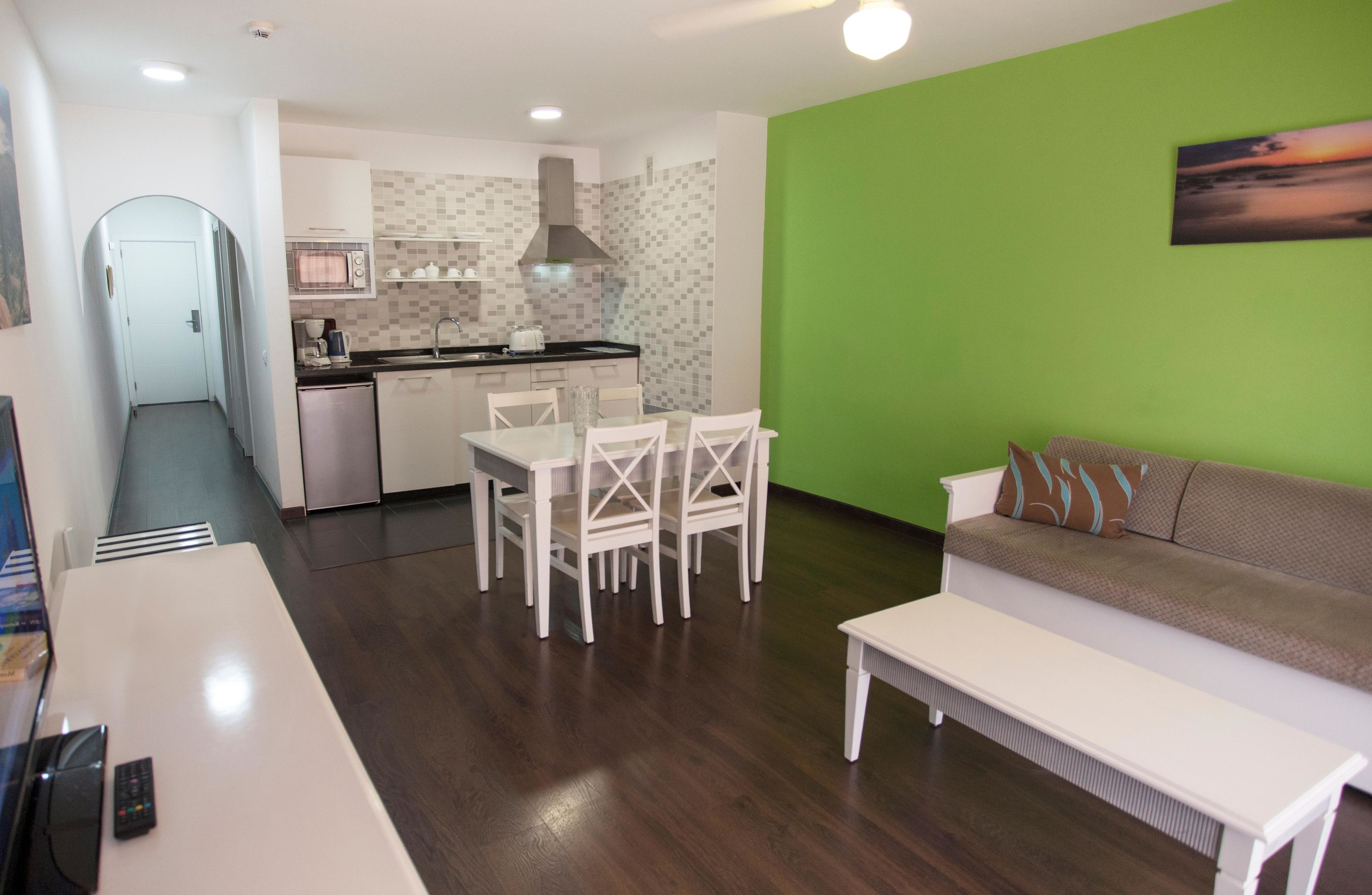 A compact living space with a kitchenette, a dining area, a sofa, and a TV.