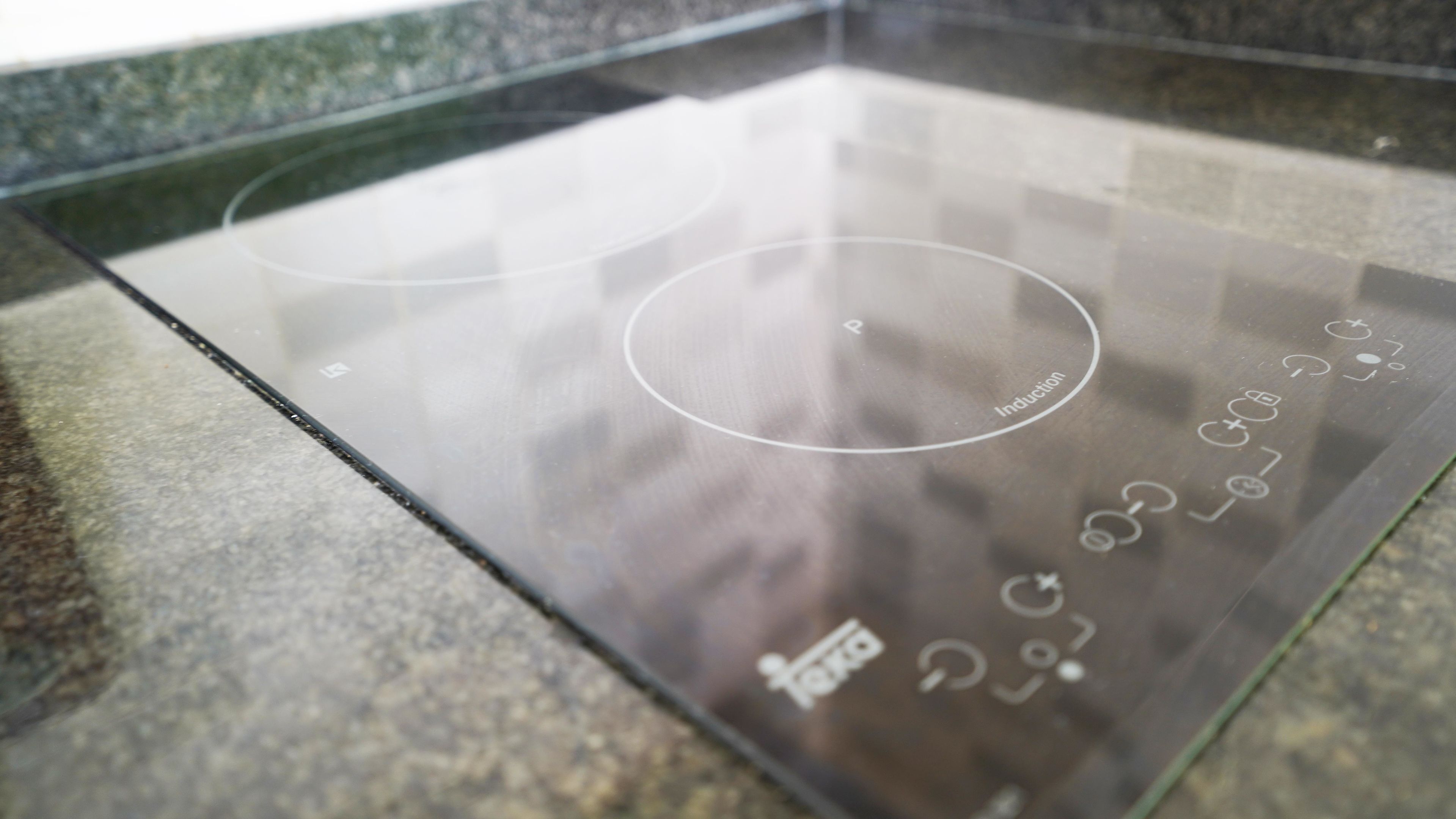 A kitchen with a glass induction cooktop, a granite countertop, and a stainless steel backsplash.