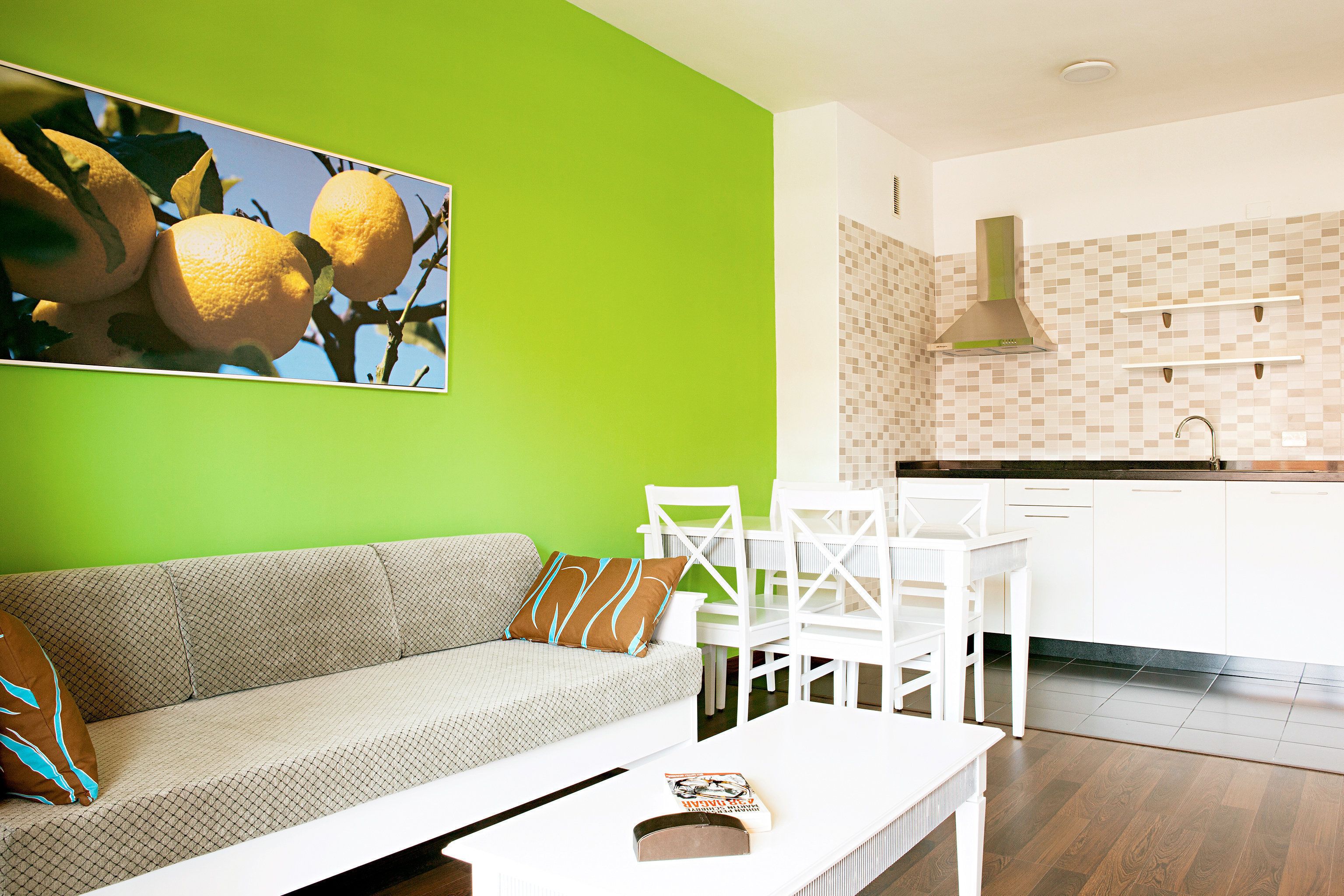 Un salon moderne avec un mur d’accent vert, un canapé blanc et un coin repas avec des chaises blanches.