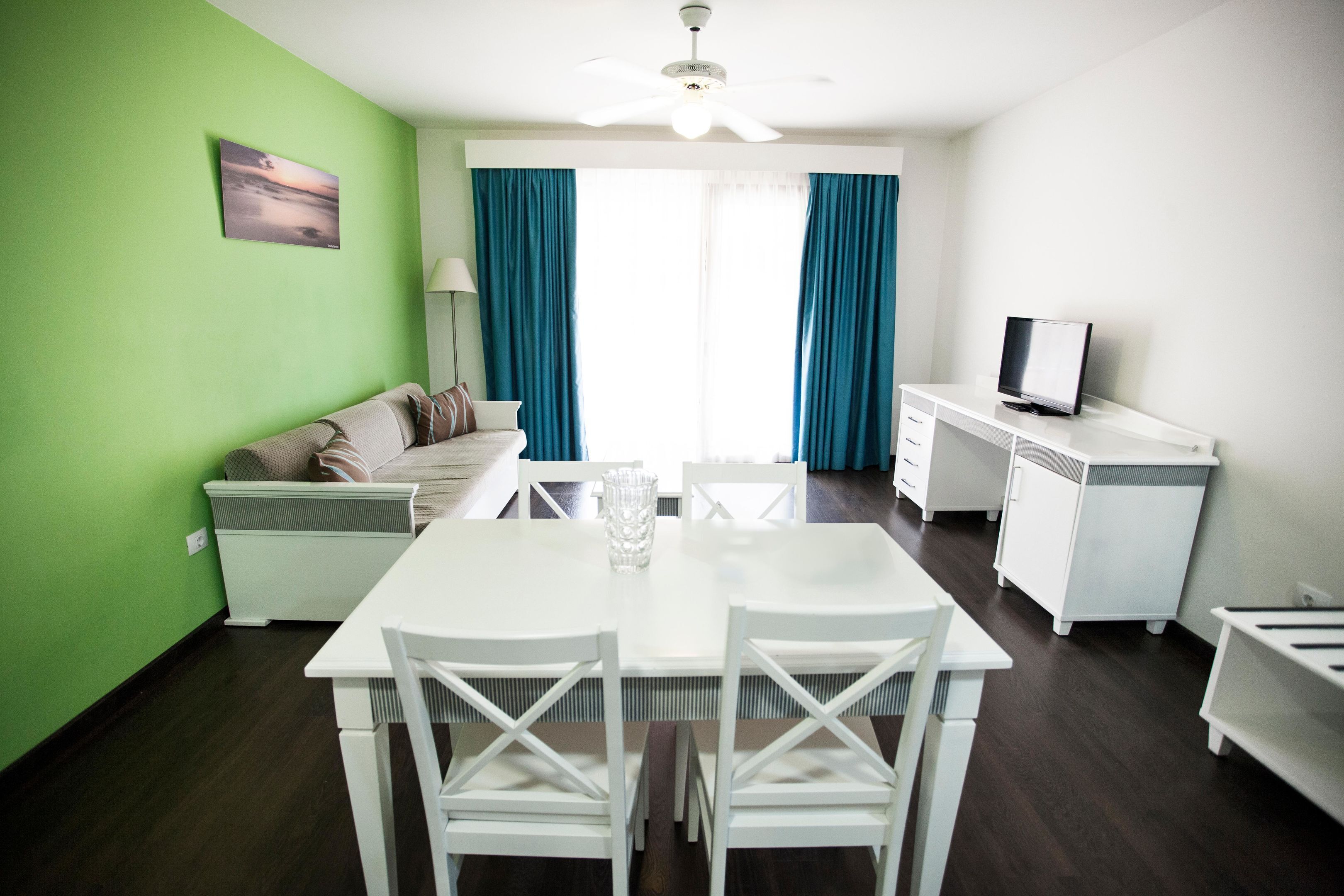 Sala de estar moderna com mesa de jantar, mobiliário branco, televisão e vista através de grandes janelas.