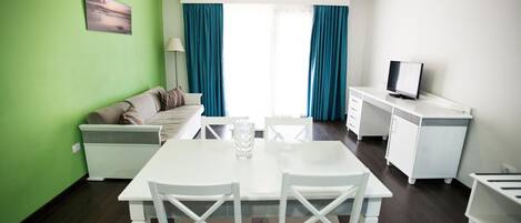 Sala de estar moderna com mesa de jantar, mobiliário branco, televisão e vista através de grandes janelas.