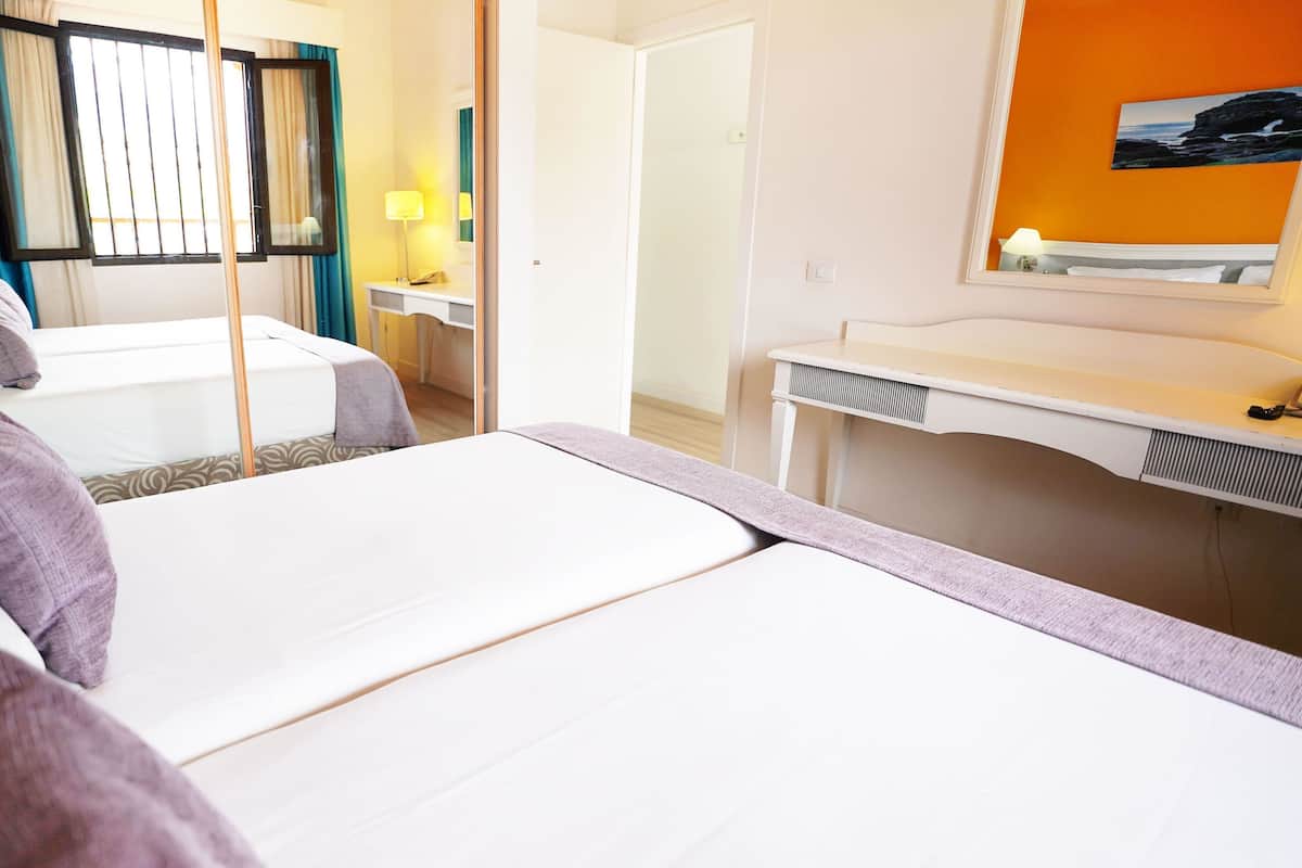 A hotel room with two beds, a desk, a mirror, and a window with curtains.