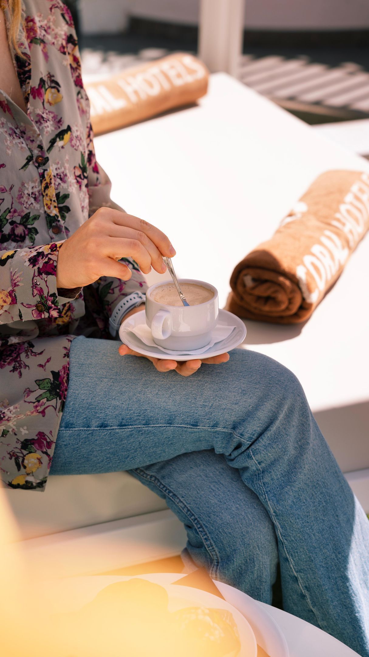 A person sitting on a white sofa with a cup of coffee on a saucer.