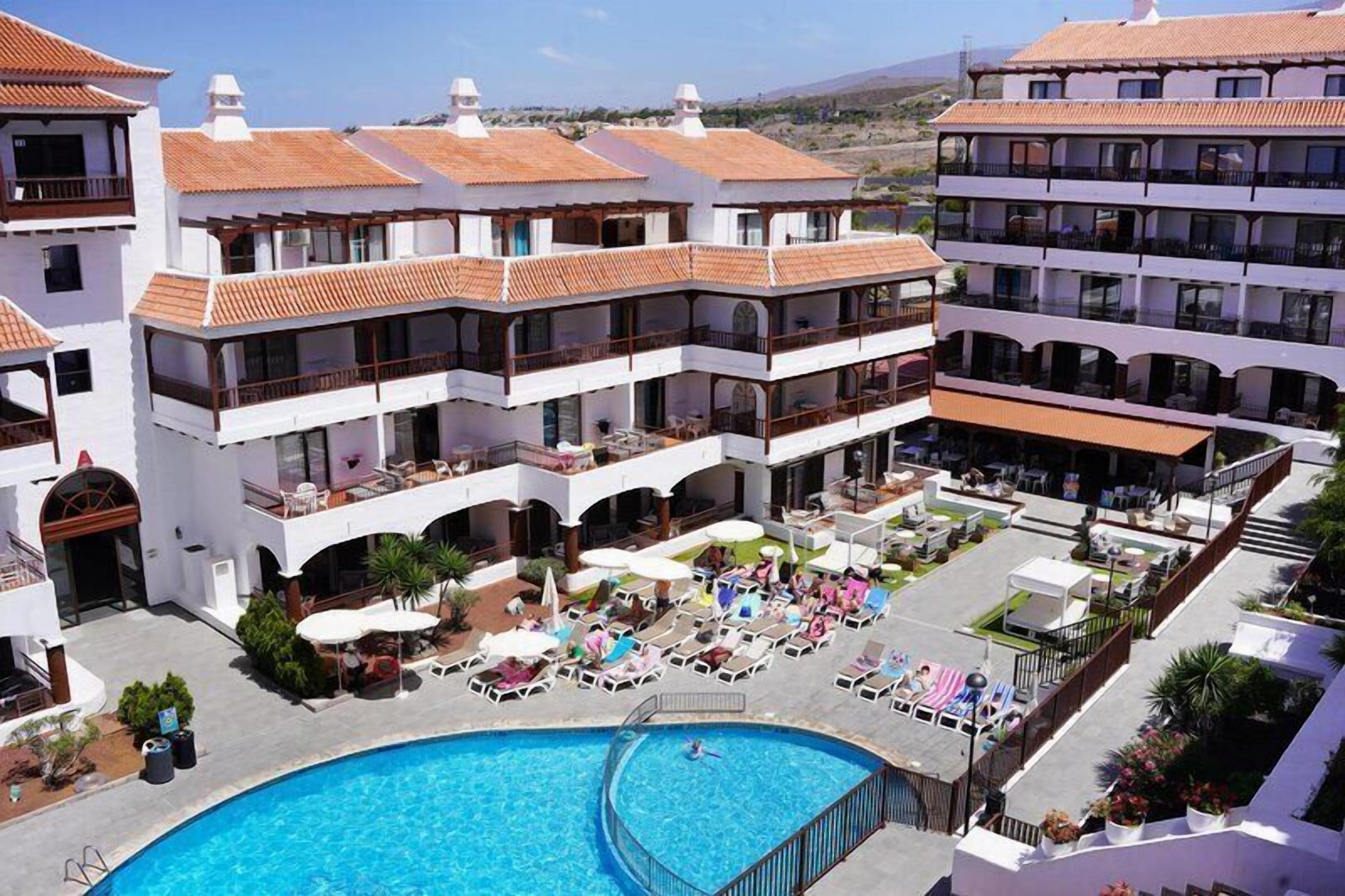 Un hotel con varios balcones, piscina y zonas de estar al aire libre.