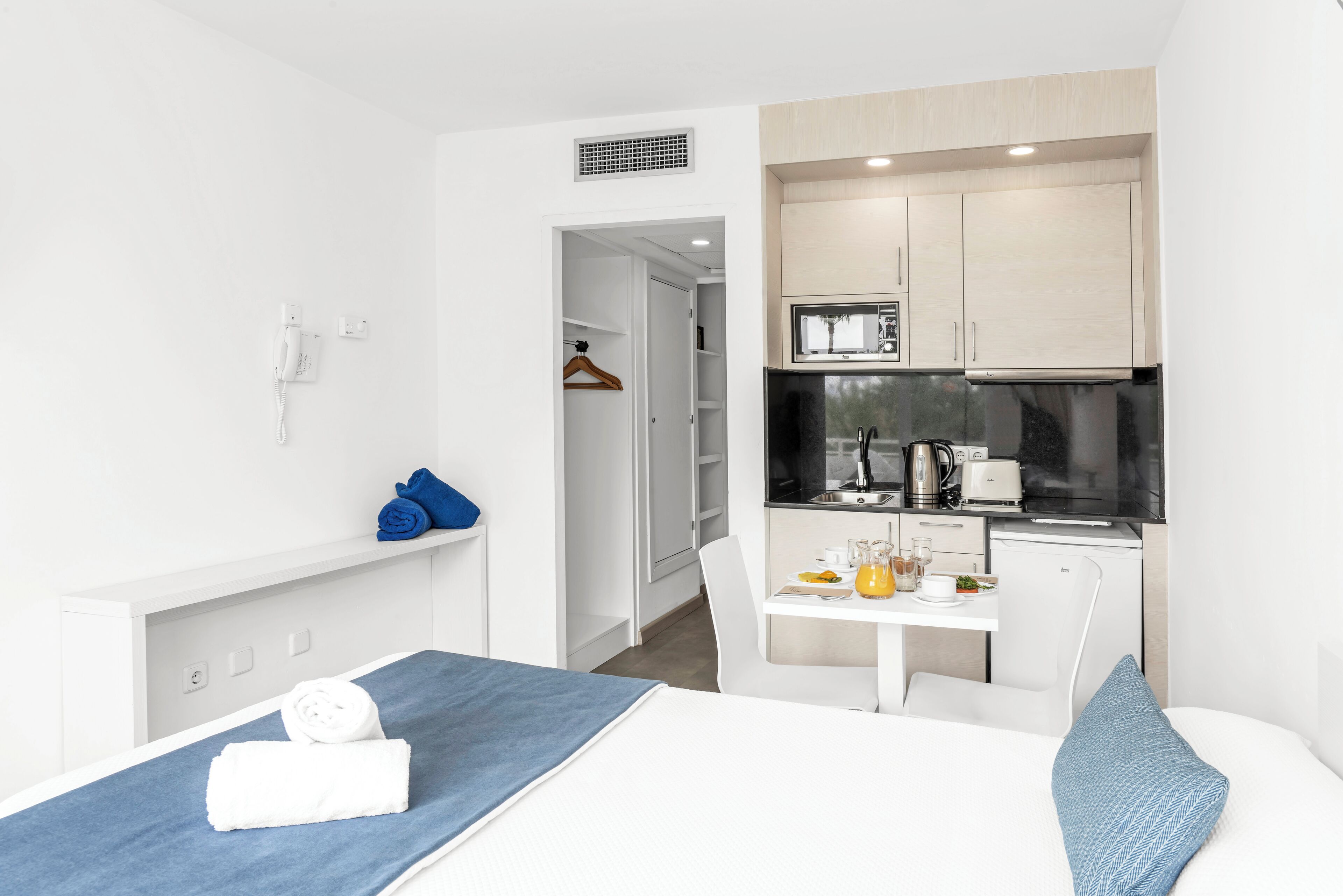 A hotel room with a bed, a small desk, a kitchenette, and a walk-in closet.