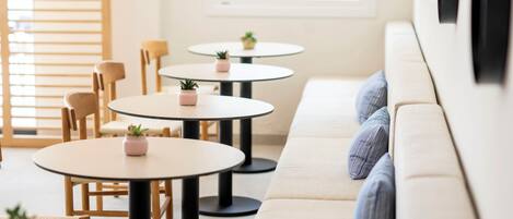 A modern interior with round tables, cushioned seating, and small potted plants.