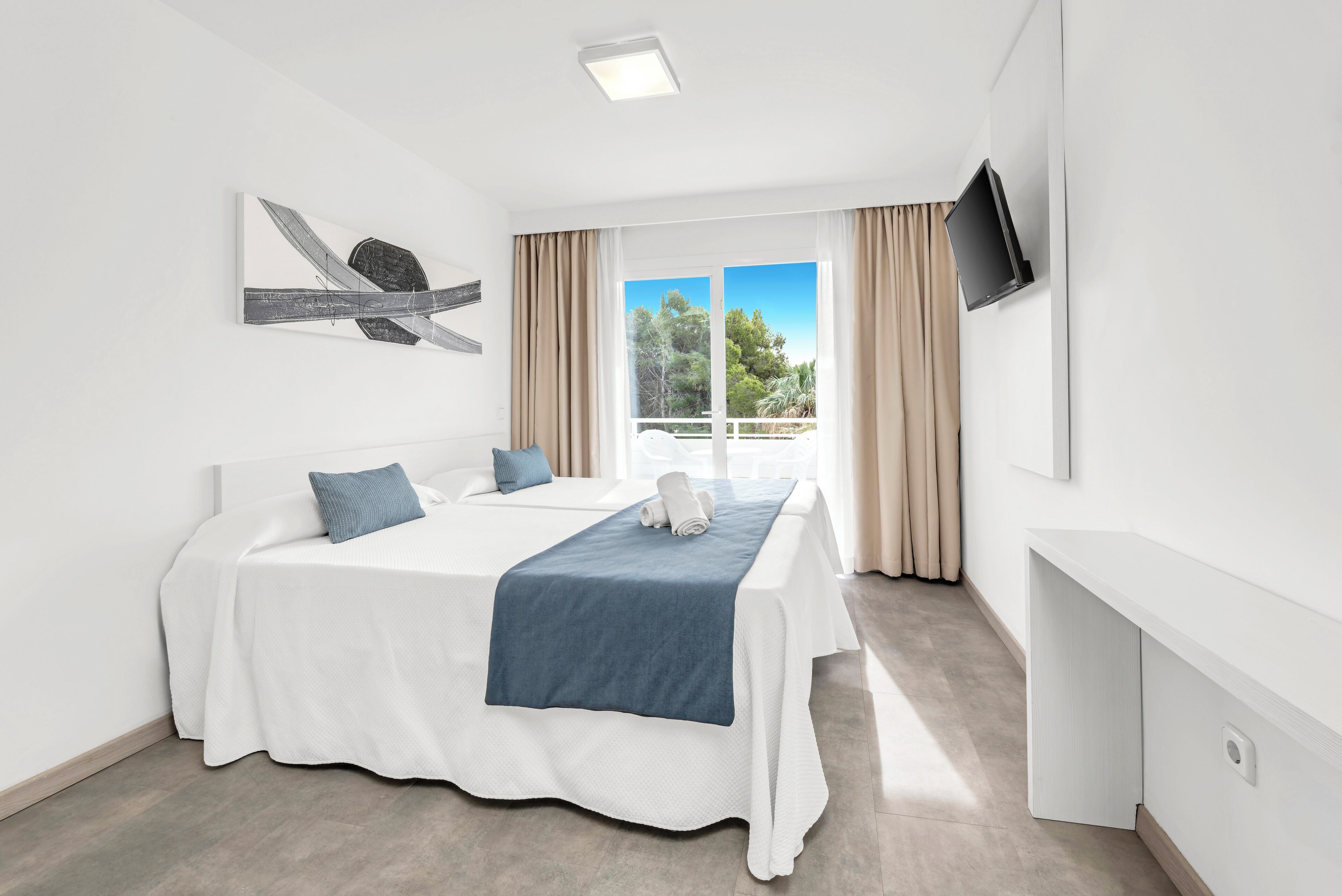 Una habitación de hotel con una cama, un televisor montado en la pared y una ventana con cortinas.