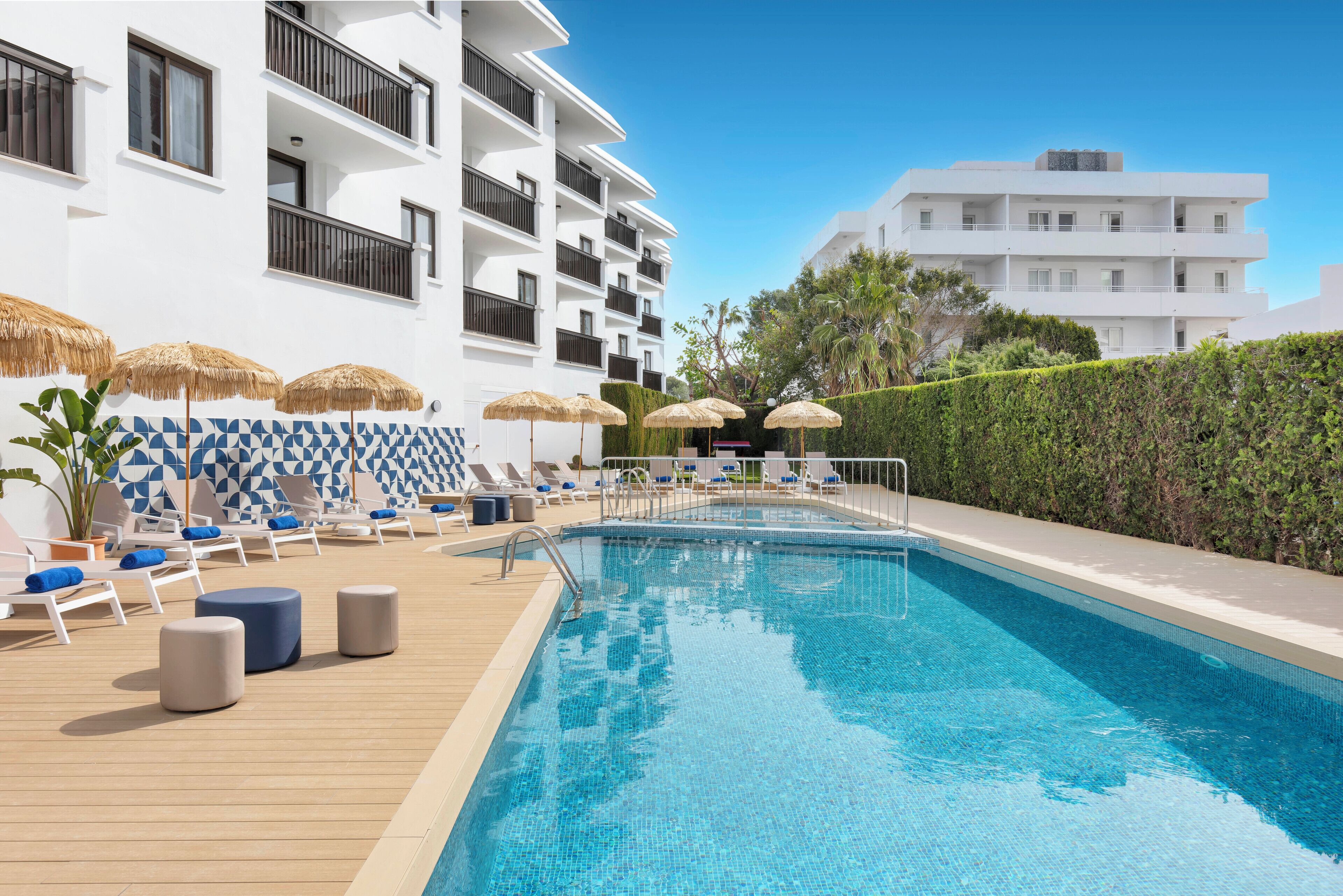 A swimming pool with lounge chairs and umbrellas, surrounded by a white building with balconies.