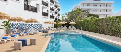 A swimming pool with lounge chairs and umbrellas, surrounded by a white building with balconies.