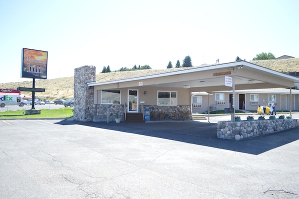 A motel with a stone facade, a covered parking area, and a signboard advertising a nearby restaurant.