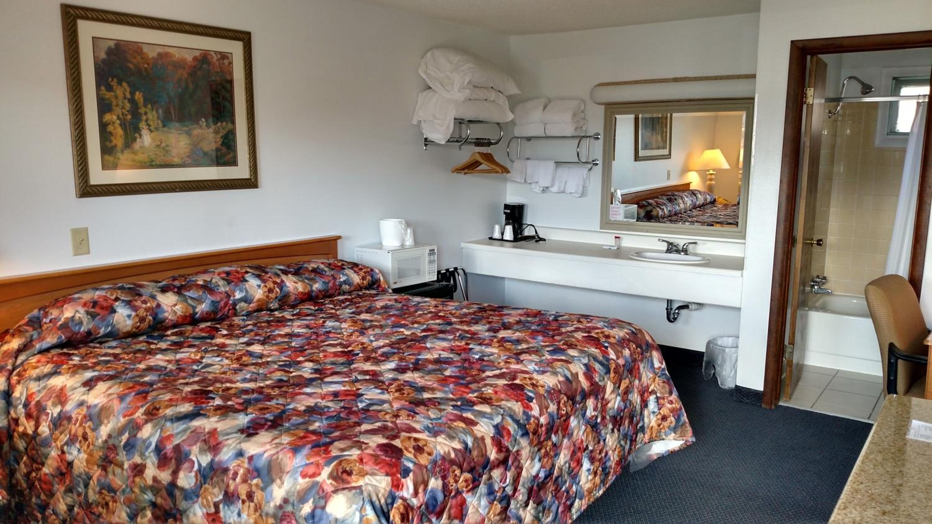 Een hotelkamer met een groot bed, een nachtkastje met een lamp, een badkamer met douche en een spiegel boven de wastafel.