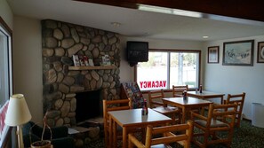 A cozy indoor setting with a stone fireplace, wooden tables and chairs, a television mounted on the wall, and a sign reading 'ACCADEMY'.
