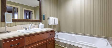 A bathroom with a wooden vanity, a sink, a mirror, a bathtub, and a towel rack.