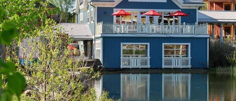 Un bâtiment au bord du lac, doté d’un balcon et de parasols rouges, dont le reflet se mire dans l’eau.