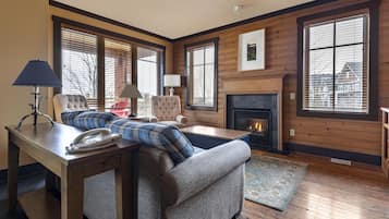 A cozy living room with a fireplace, a sofa, a chair, and a table with a lamp and a phone.