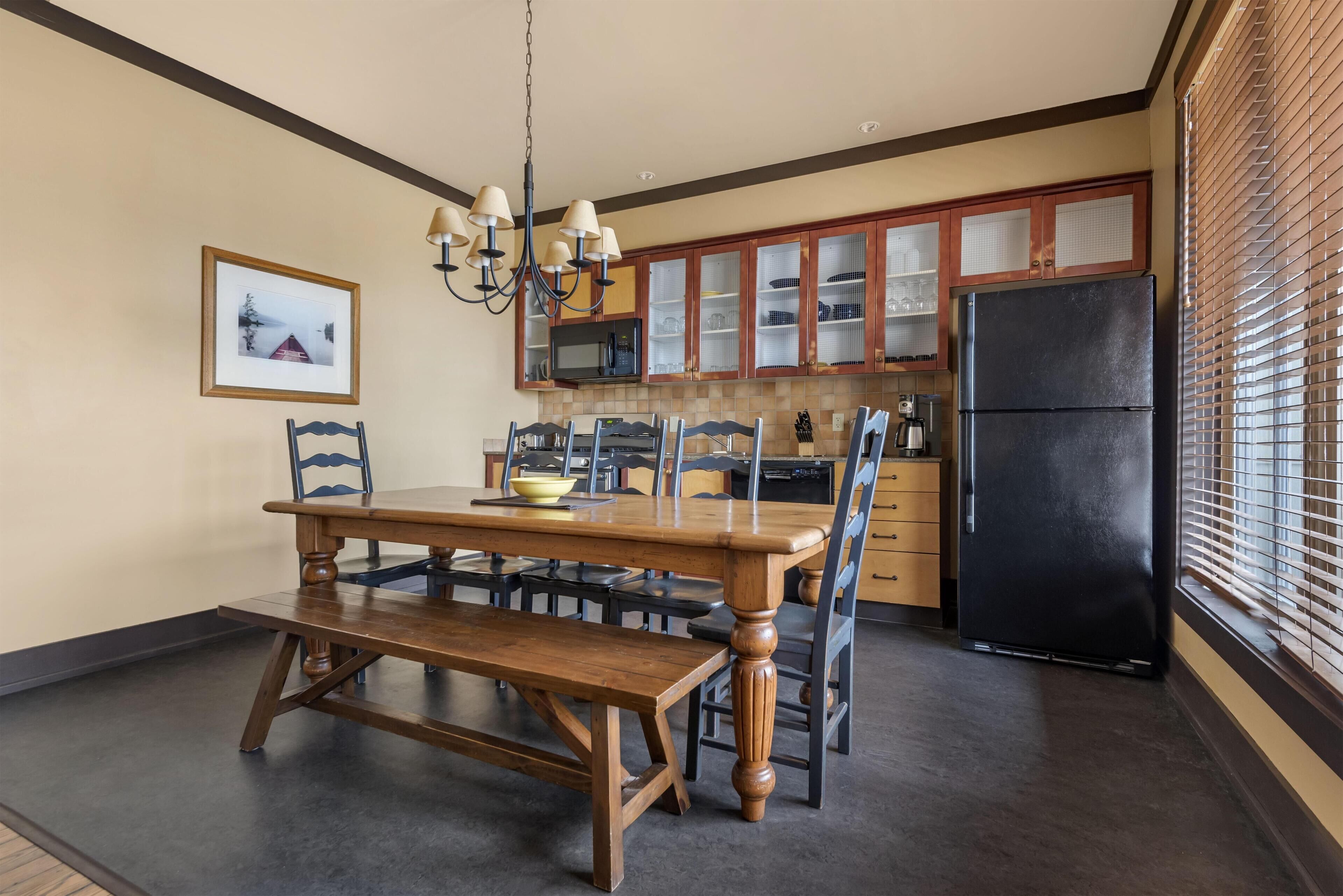A dining area with a wooden table and chairs, a chandelier, and a black refrigerator.