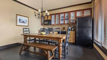 A dining area with a wooden table and chairs, a chandelier, and a black refrigerator.