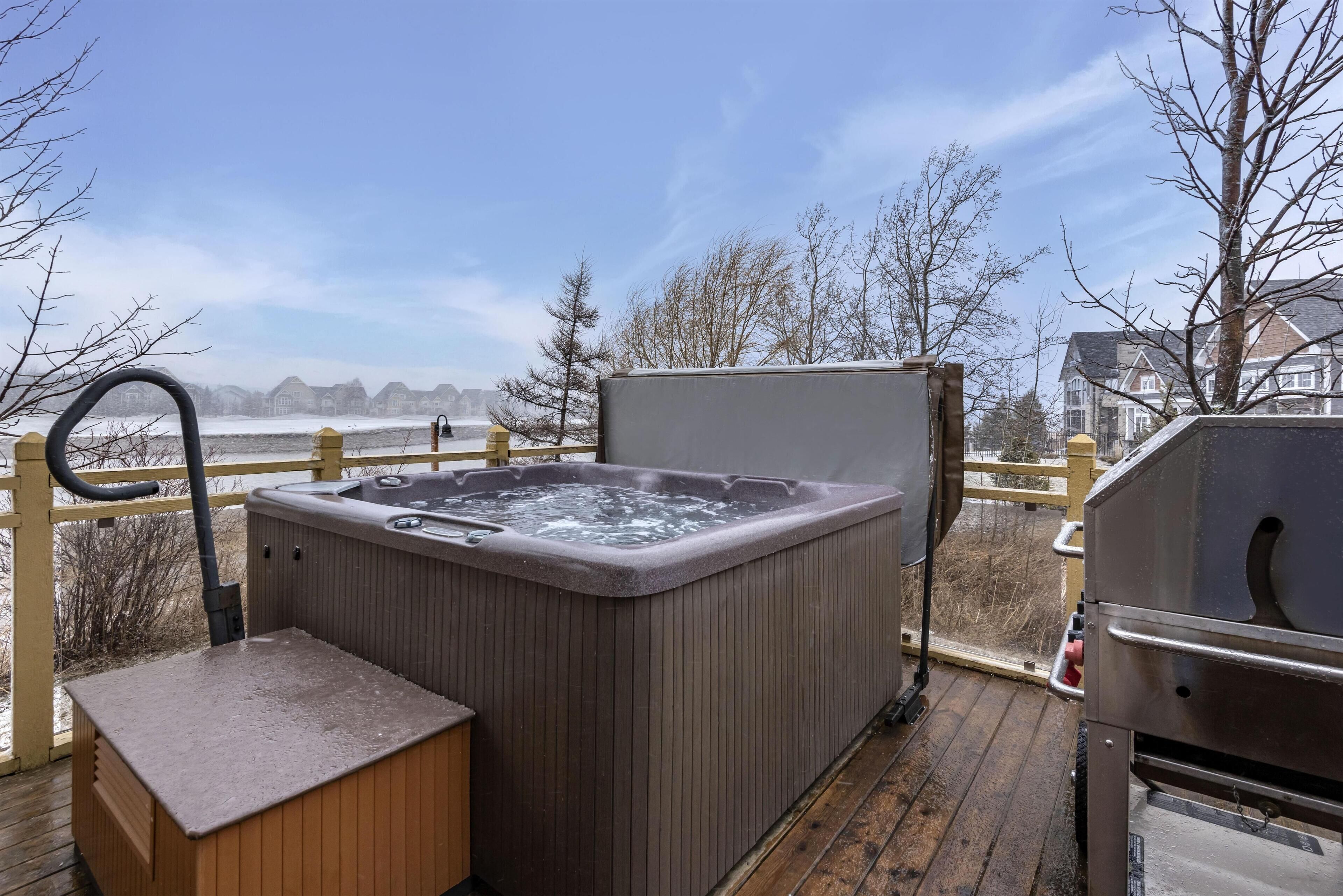 Un jacuzzi en una terraza de madera con vistas a casas y árboles al fondo.