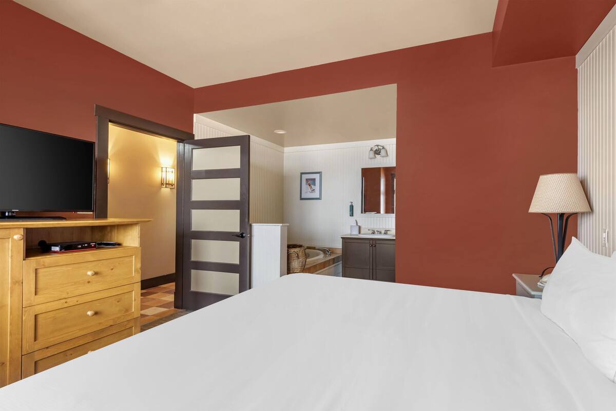 Habitación de hotel con cama, cómoda de madera, televisor y baño visible a través de una puerta abierta.