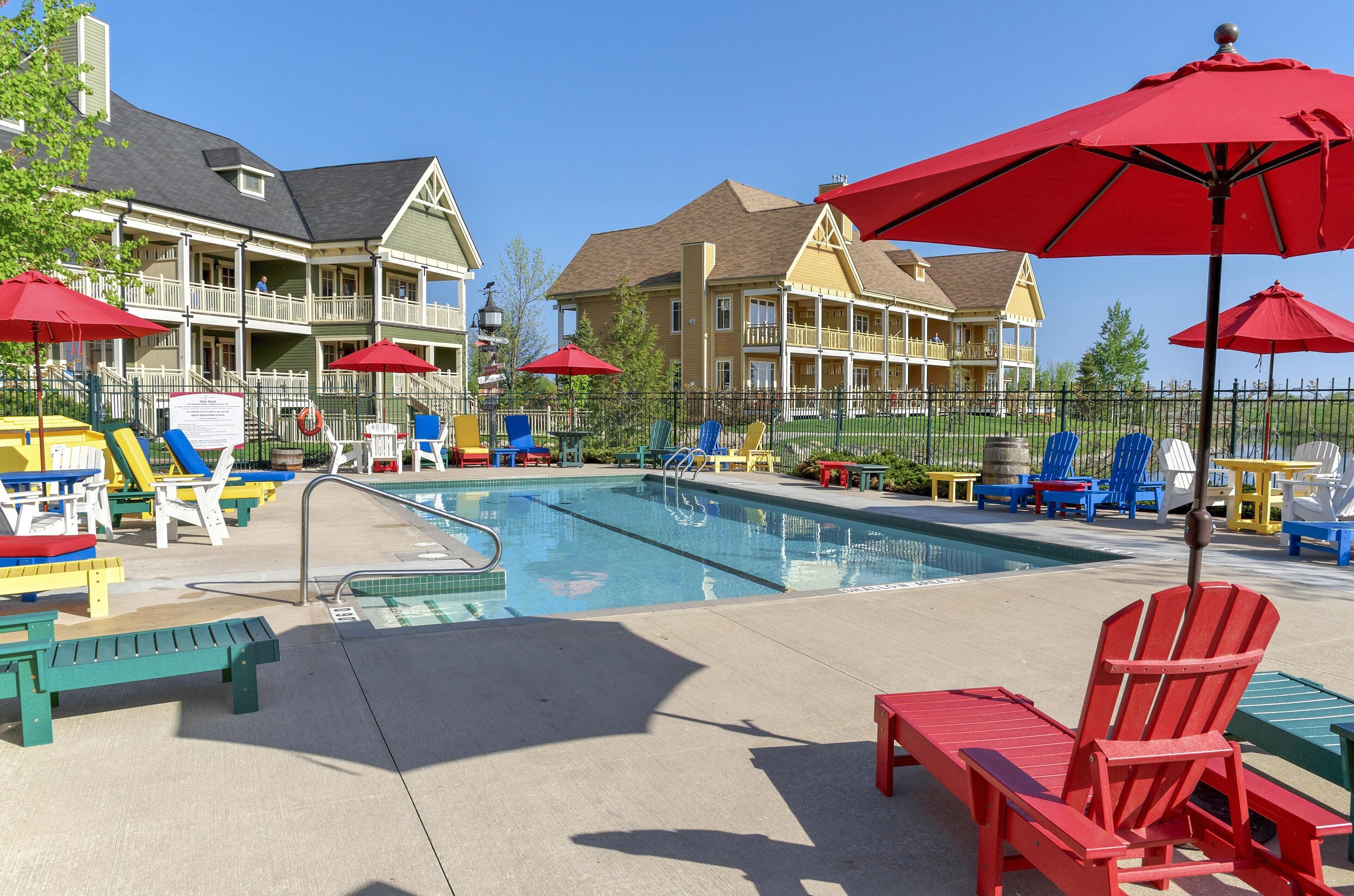 A pool area with lounge chairs and umbrellas, a pool with a diving board, and a building with balconies in the background.
