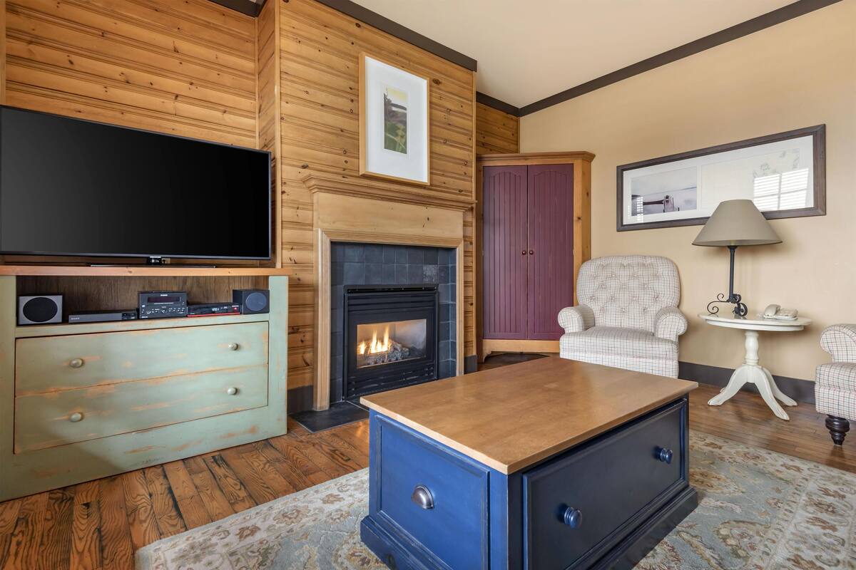 Una sala de estar con televisor, chimenea, aparador azul y sillón estampado.