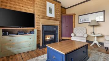 Una sala de estar con televisor, chimenea, aparador azul y sillón estampado.
