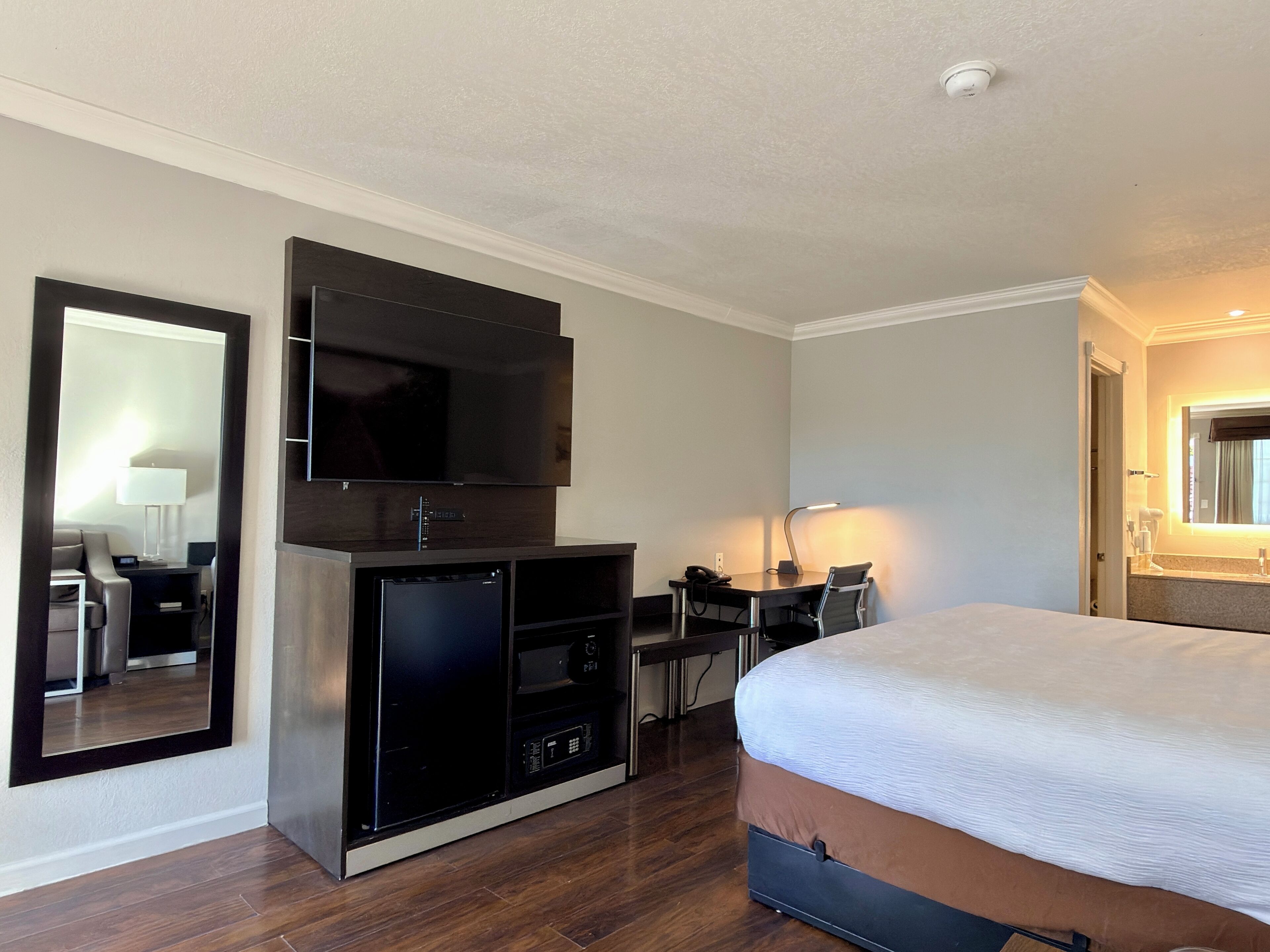 Habitació d'hotel amb un llit gran, televisió de pantalla plana, escriptori amb cadira i un mirall.