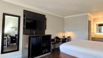 A hotel room with a large bed, a flat-screen TV, a desk with a chair, and a mirror.