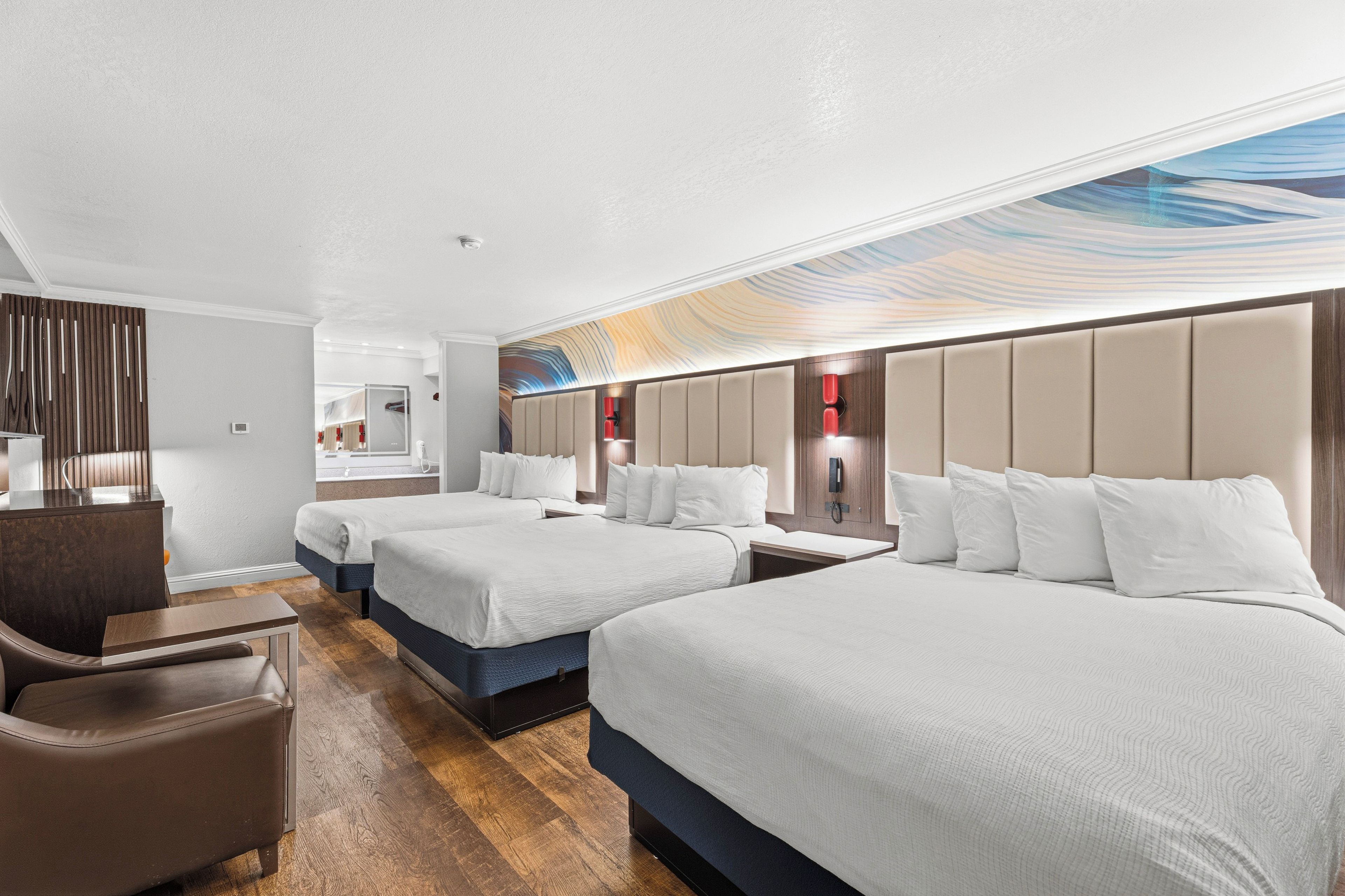 A hotel room with two beds, a desk, a chair, and a bathroom visible in the background.