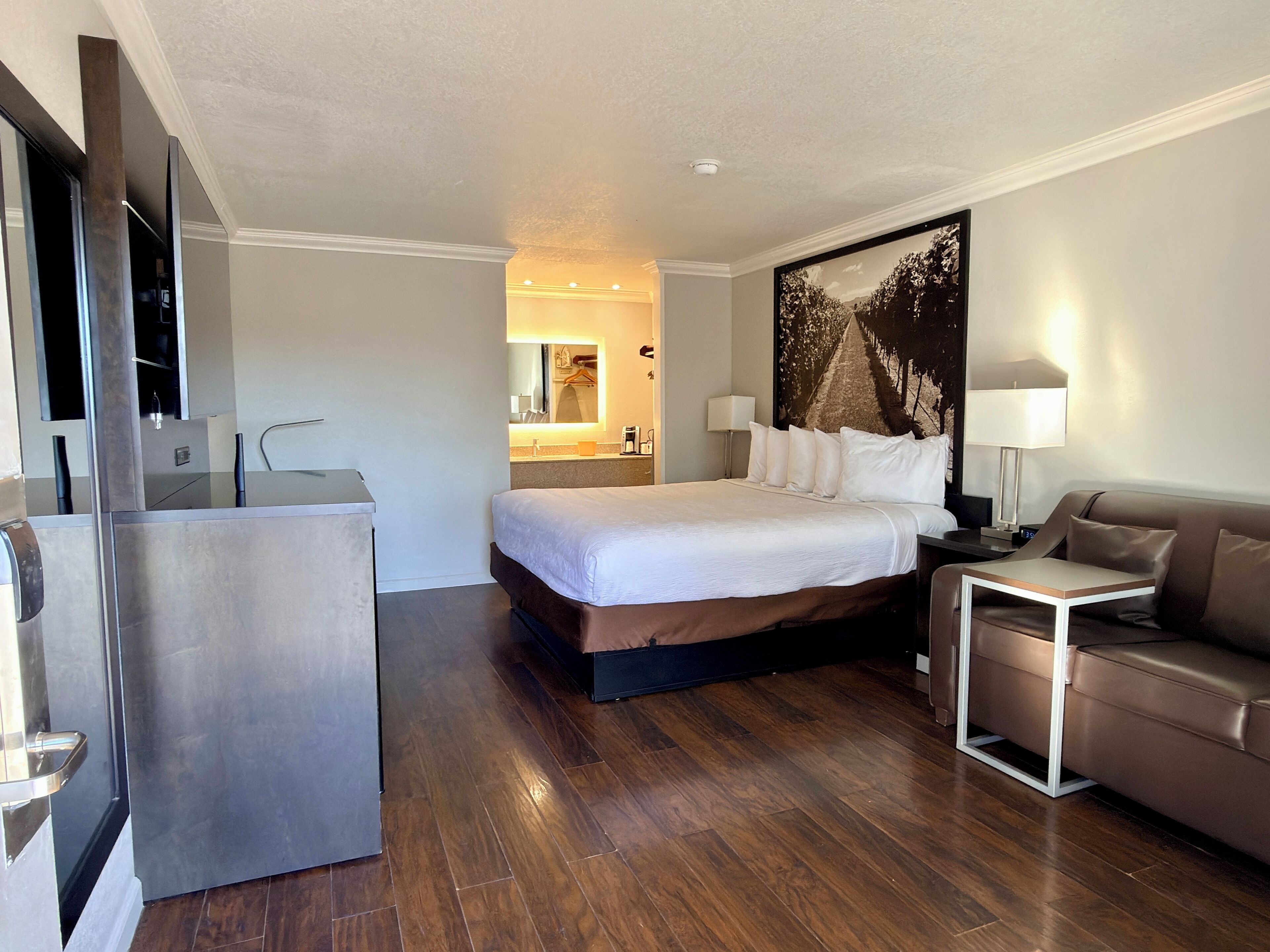 Een moderne hotelkamer met een groot bed, een bureau, een bank en een badkamer zichtbaar door een geopende deur.