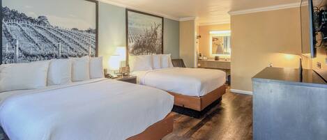Habitación de hotel con dos camas, un espejo grande, suelo de madera y vistas a un viñedo.