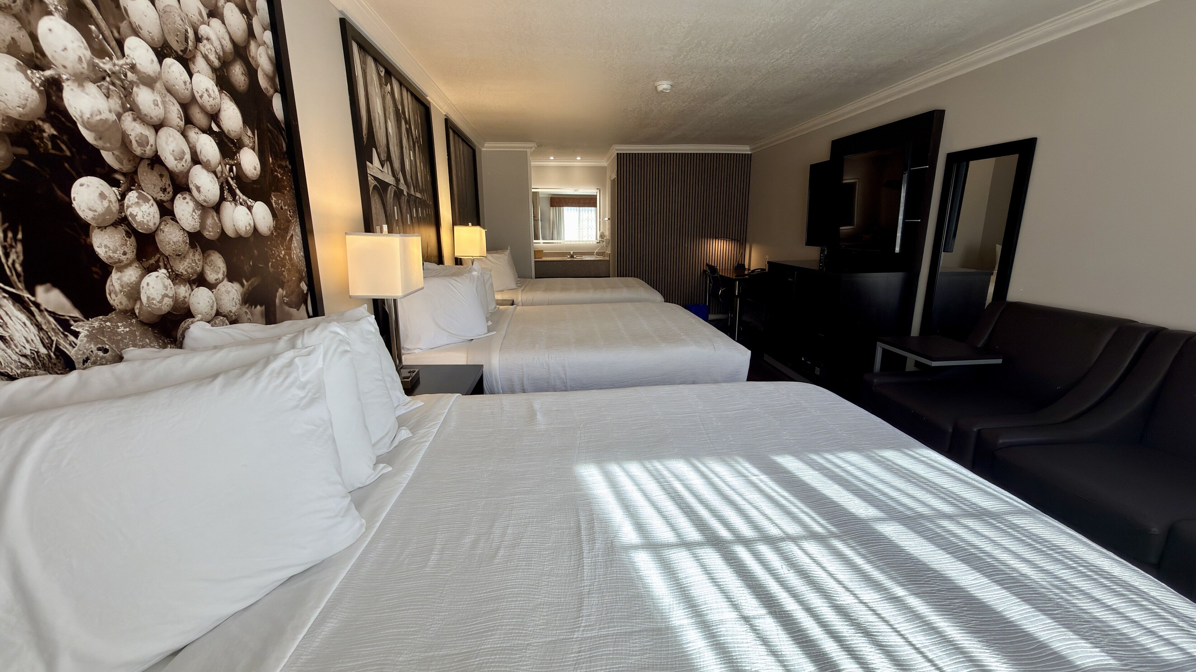 A hotel room with two beds, a large wall mural, a flat-screen TV, and a seating area.