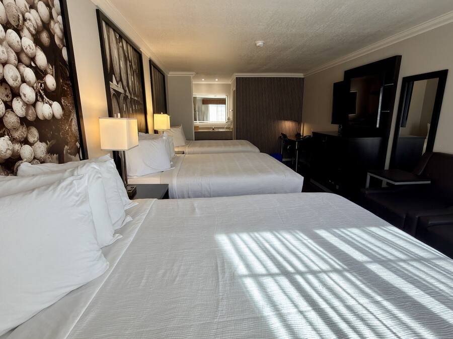 A hotel room with two beds, a large wall mural, a flat-screen TV, and a seating area.