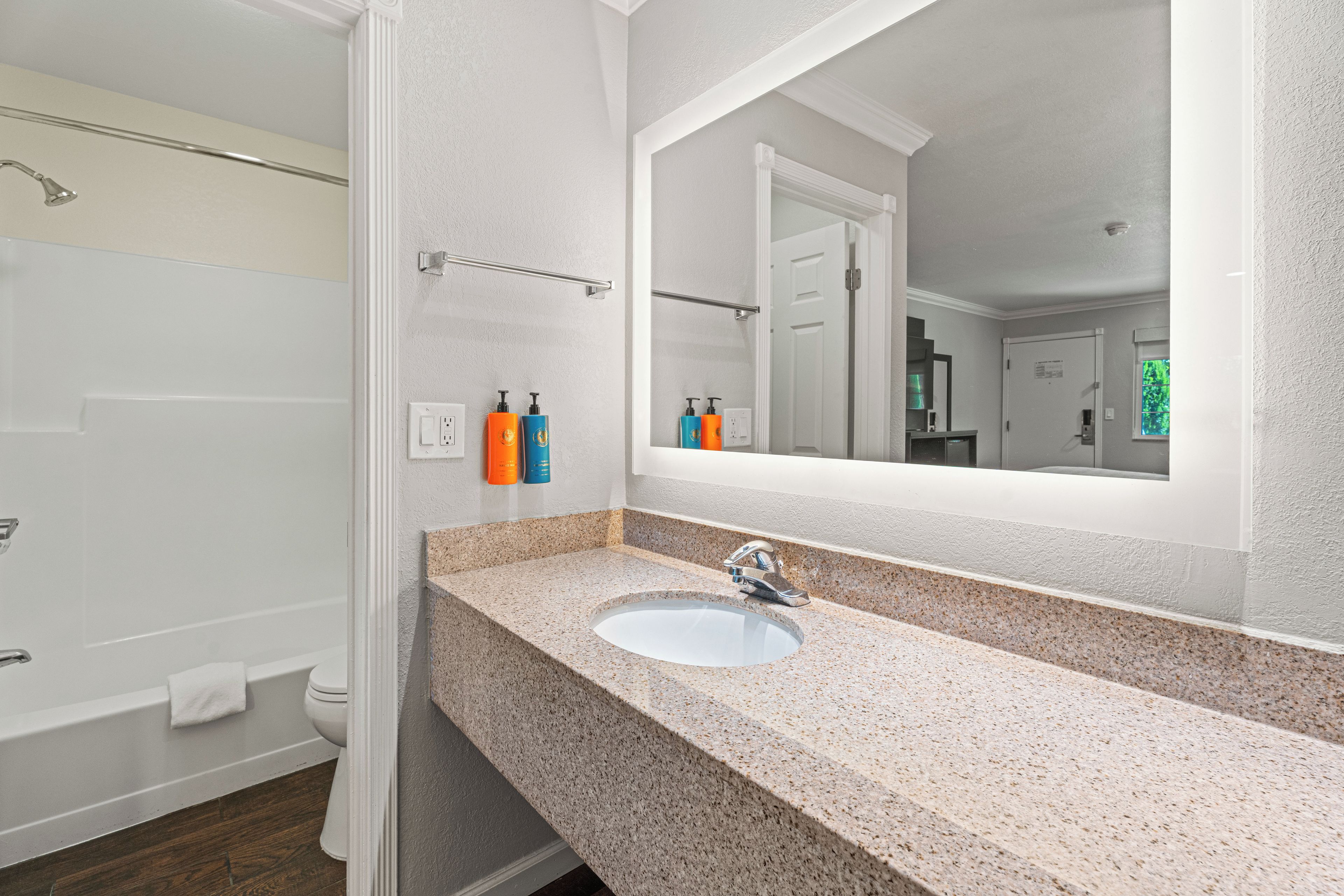 A bathroom with a granite countertop, a sink, a mirror, and a shower area.