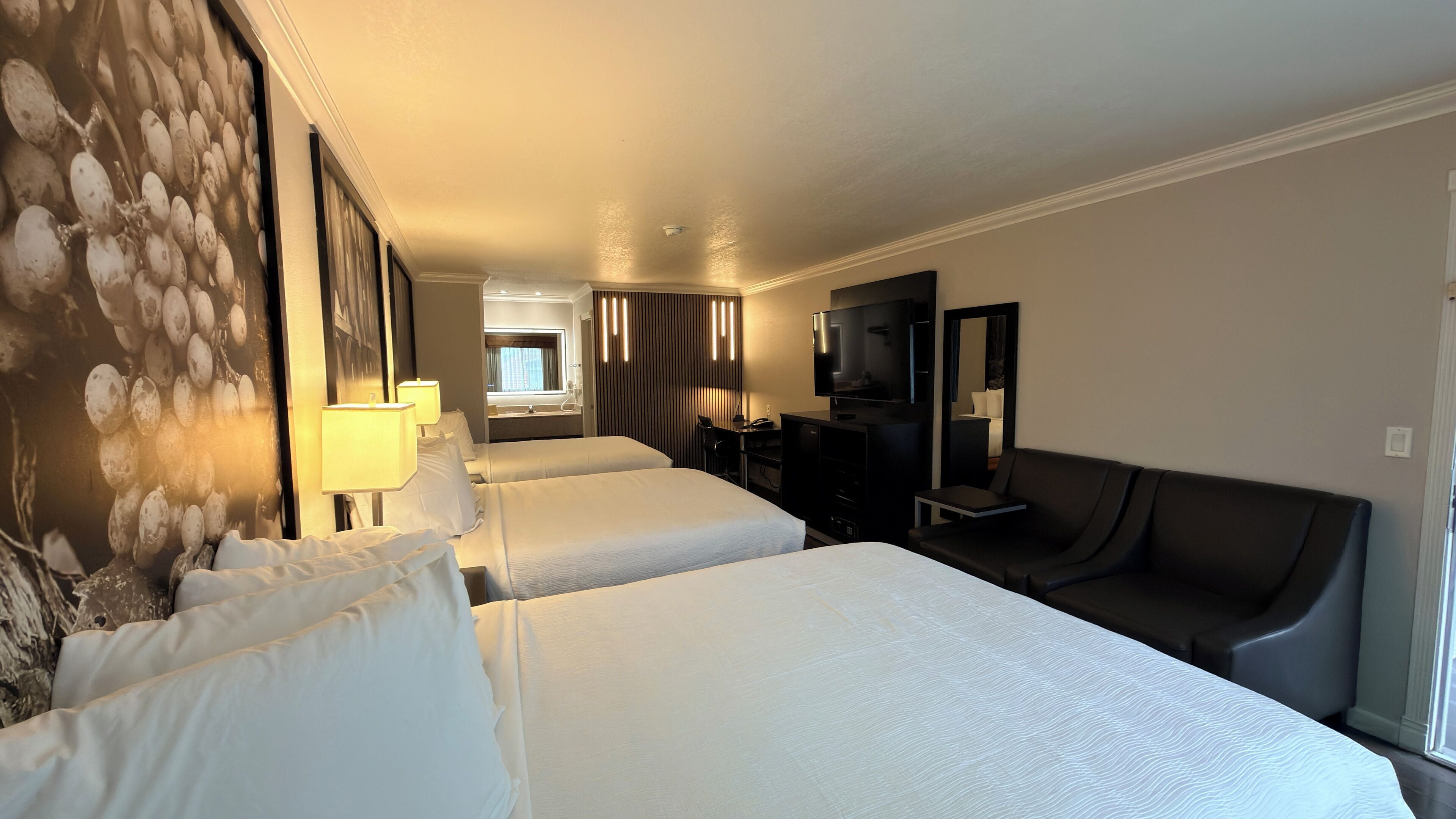 A hotel room with two beds, a TV, a desk, and a sofa.