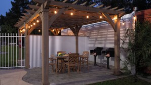 Un patio cubierto con una pérgola de madera, mobiliario exterior y una parrilla.