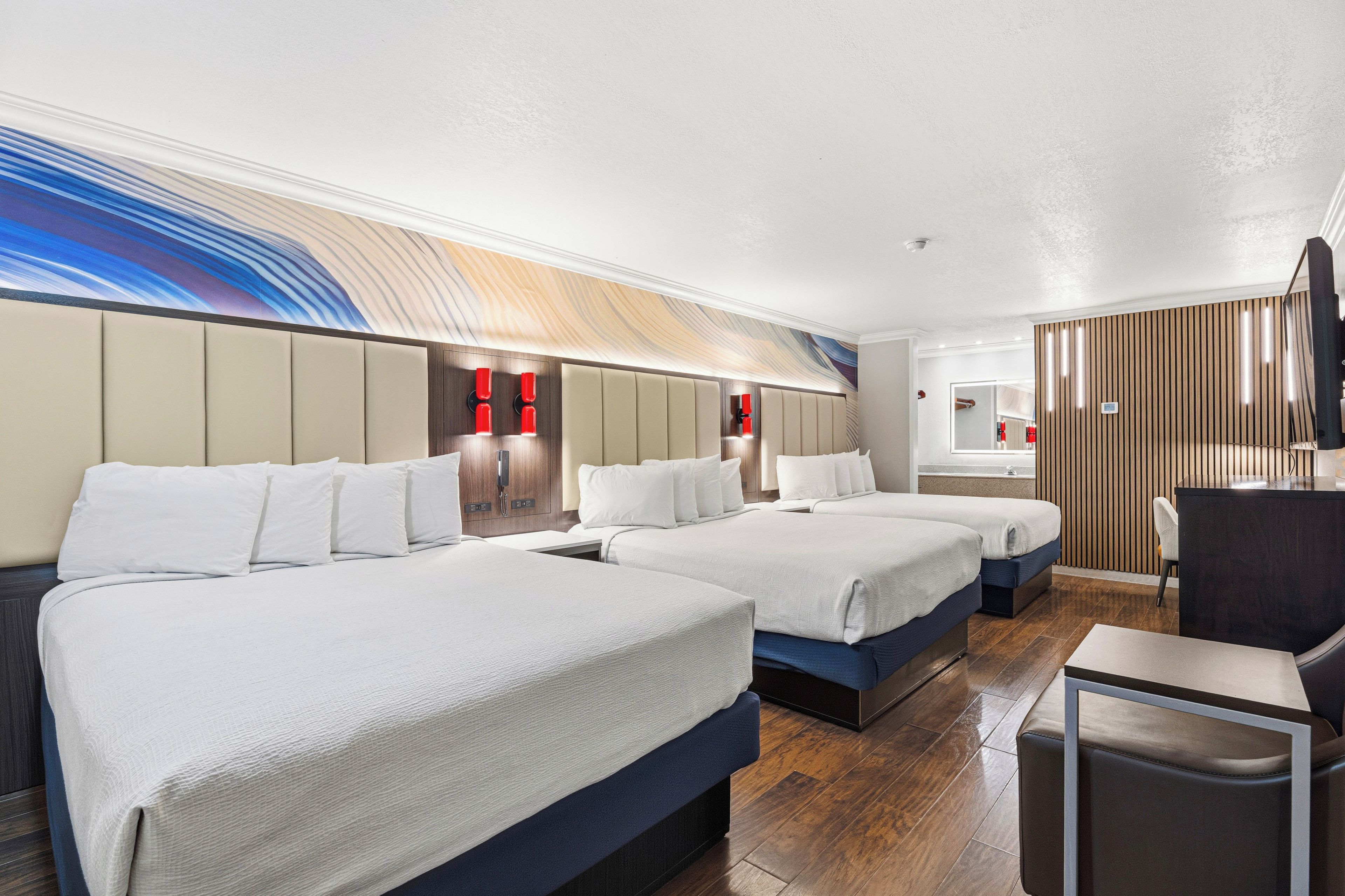 A hotel room with three beds, a desk, and a mirror.