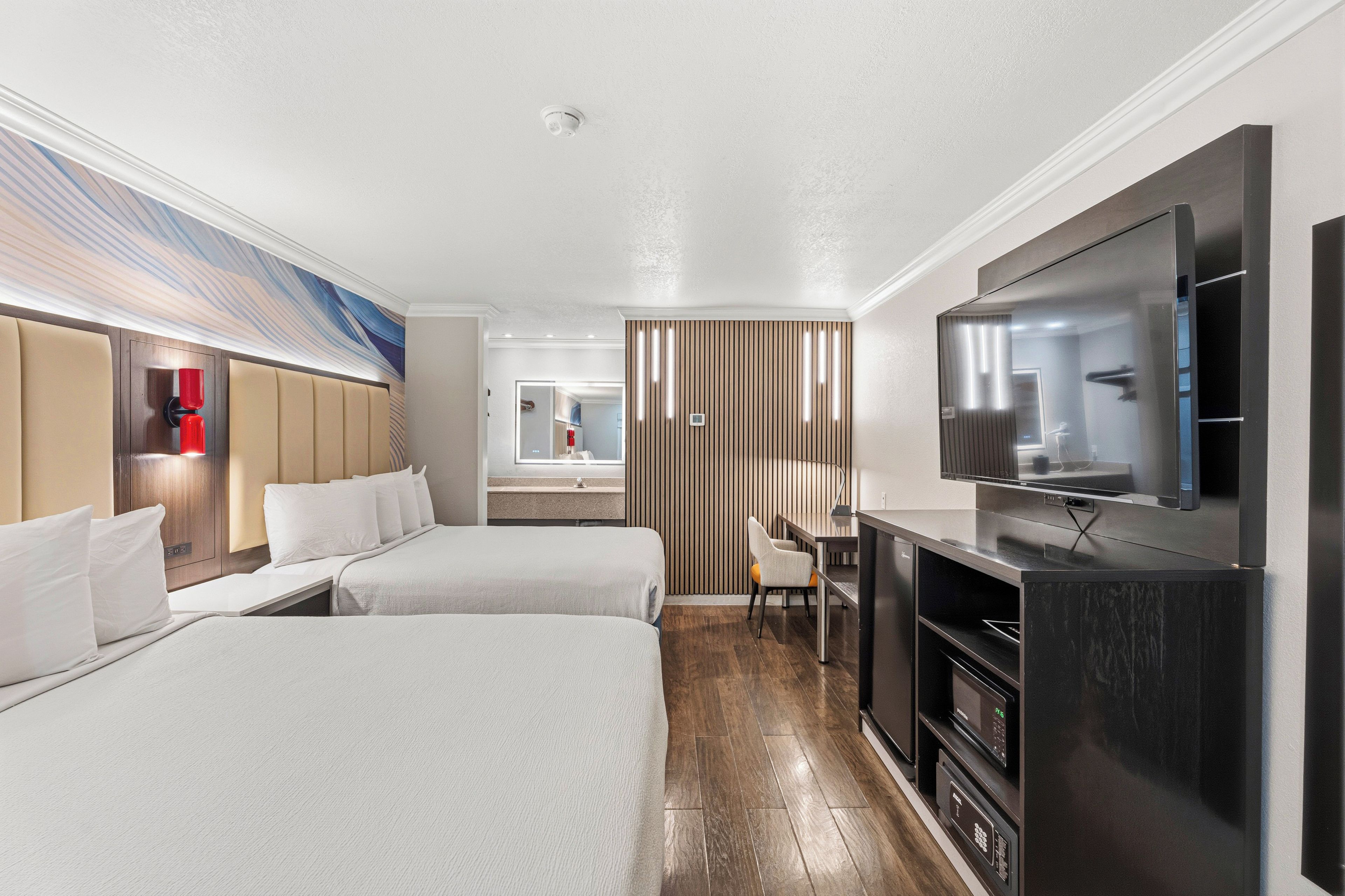 A hotel room with two beds, a TV, a desk, and a bathroom visible through a sliding door.