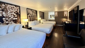 Habitación de hotel con dos camas, un escritorio, un televisor y un ventanal grande.