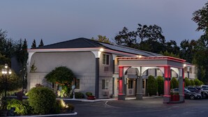 Un hotel moderno con entrada cubierta, jardines ajardinados y un área de estacionamiento.