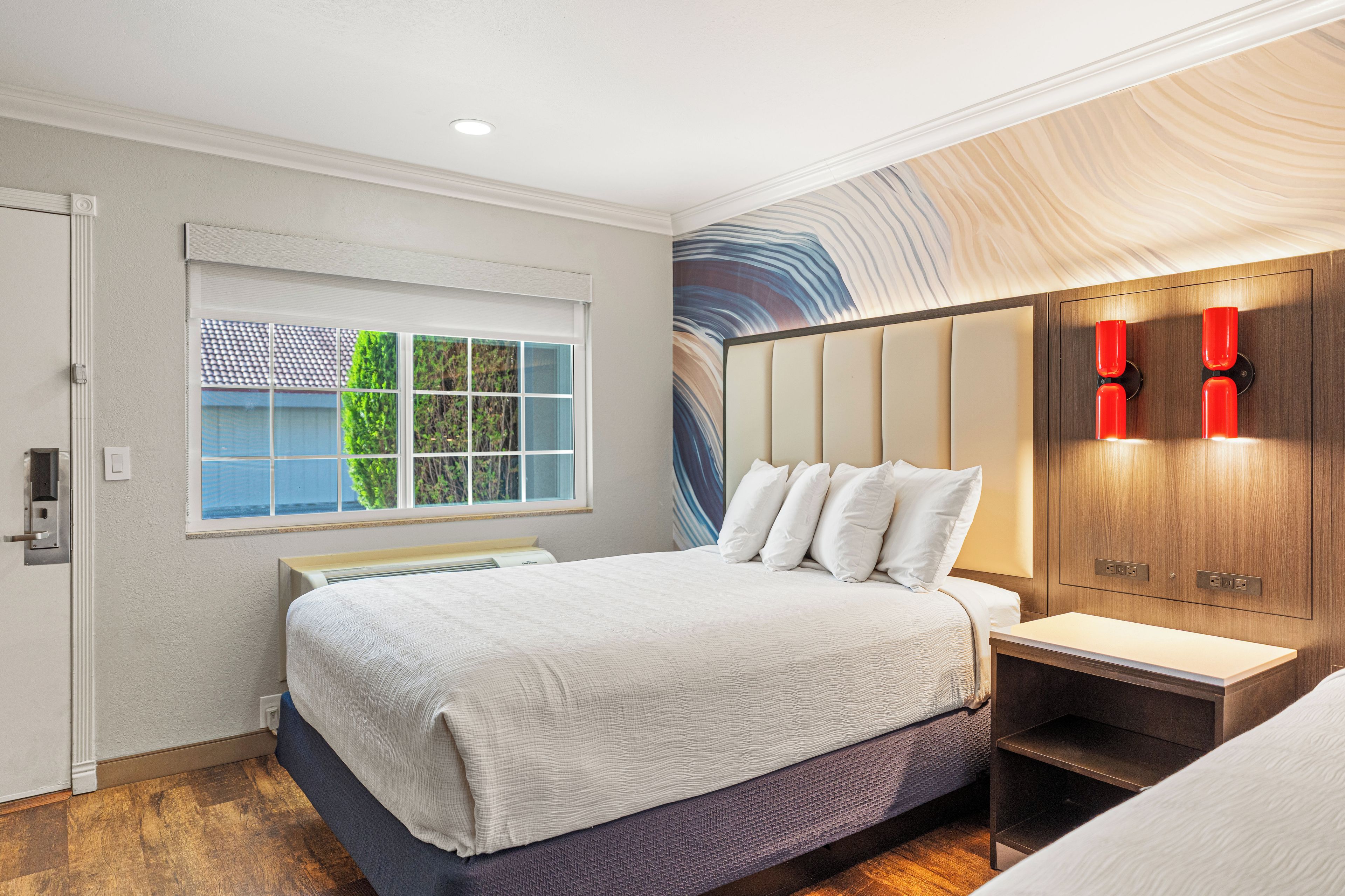 A modern bedroom with a bed, bedside table, and a view of the outdoors through a window.