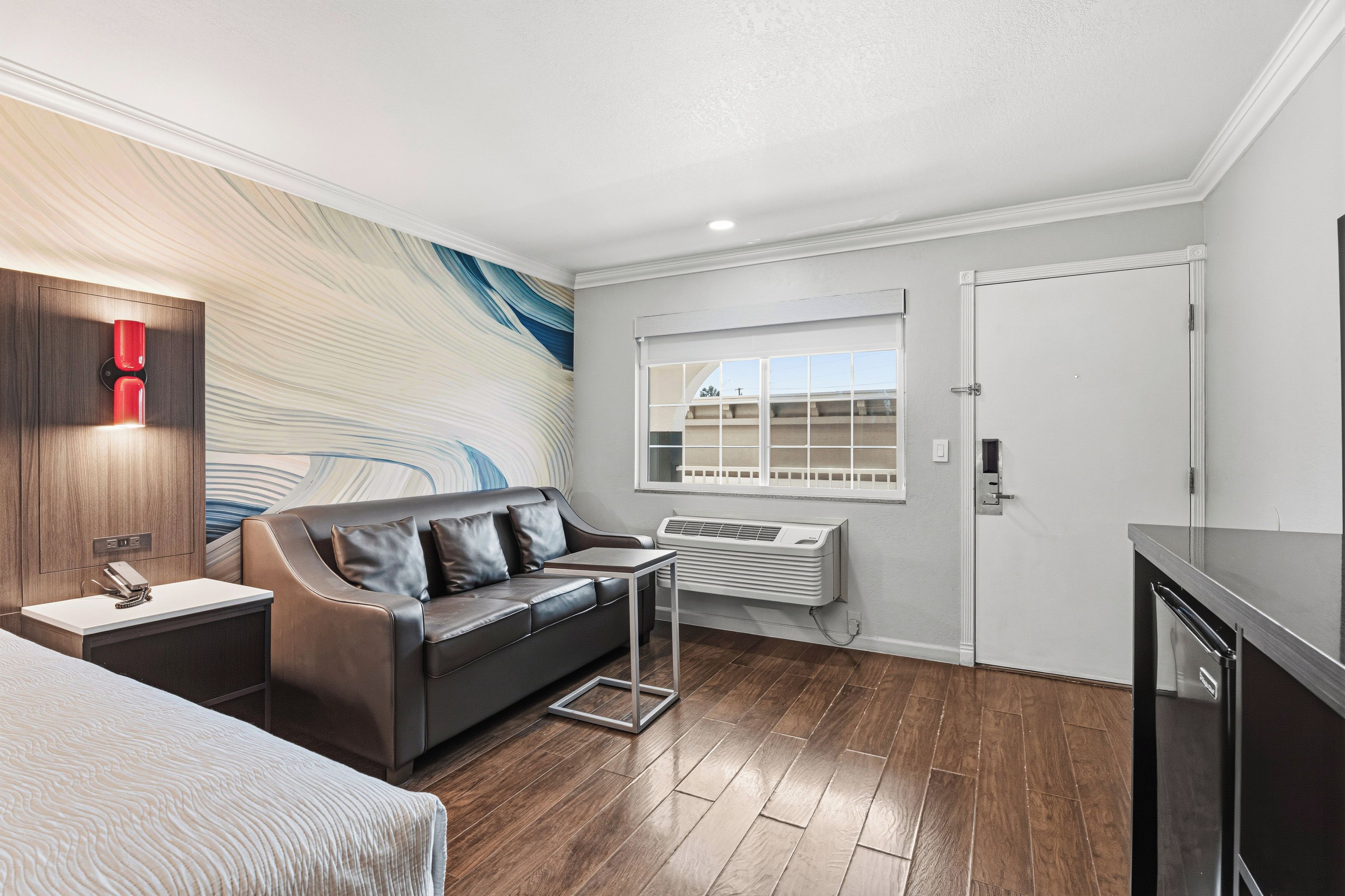 A modern hotel room with a sofa, a small table, a window with a view, and a door.