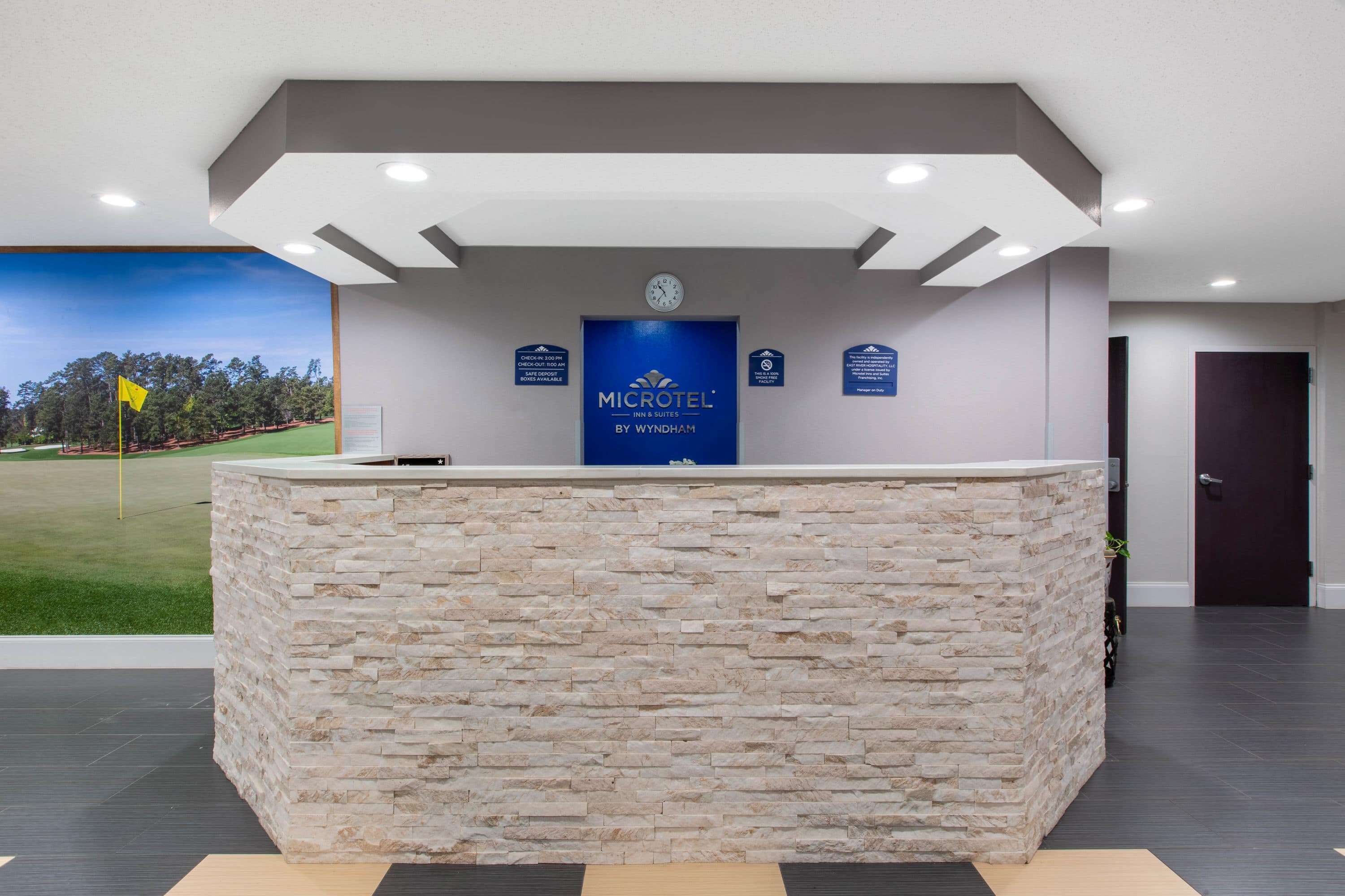 Ein Empfangsschalter mit Steinverkleidung, eine Uhr und ein Schild mit der Aufschrift 'MICROTEL INN & SUITES BY WYNDHAM'.