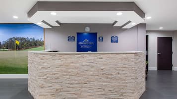 Ein Empfangsschalter mit Steinverkleidung, eine Uhr und ein Schild mit der Aufschrift 'MICROTEL INN & SUITES BY WYNDHAM'.