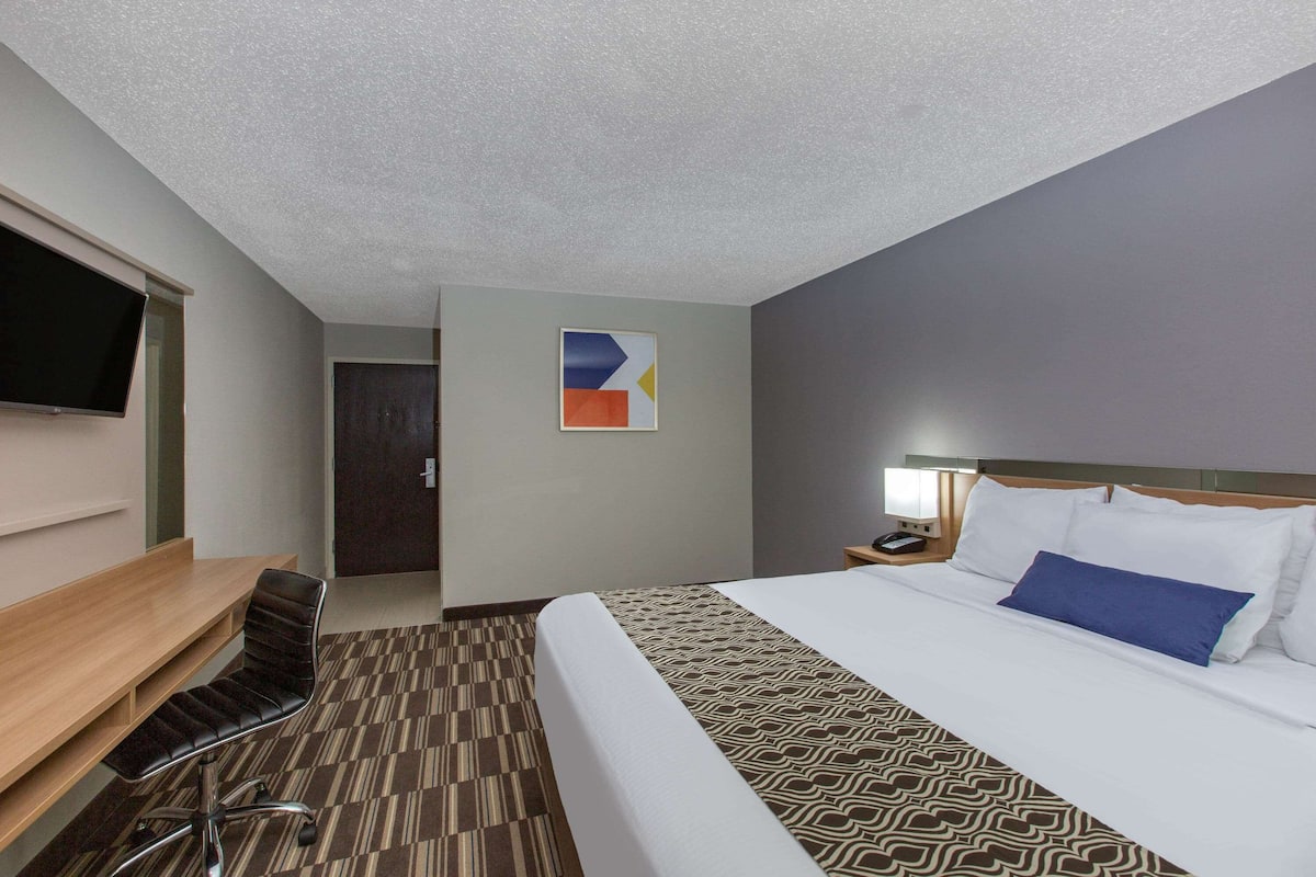 A hotel room with a bed, a desk, a chair, a television, and a door.