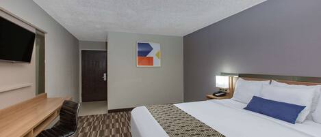 A hotel room with a bed, a desk, a chair, a television, and a door.