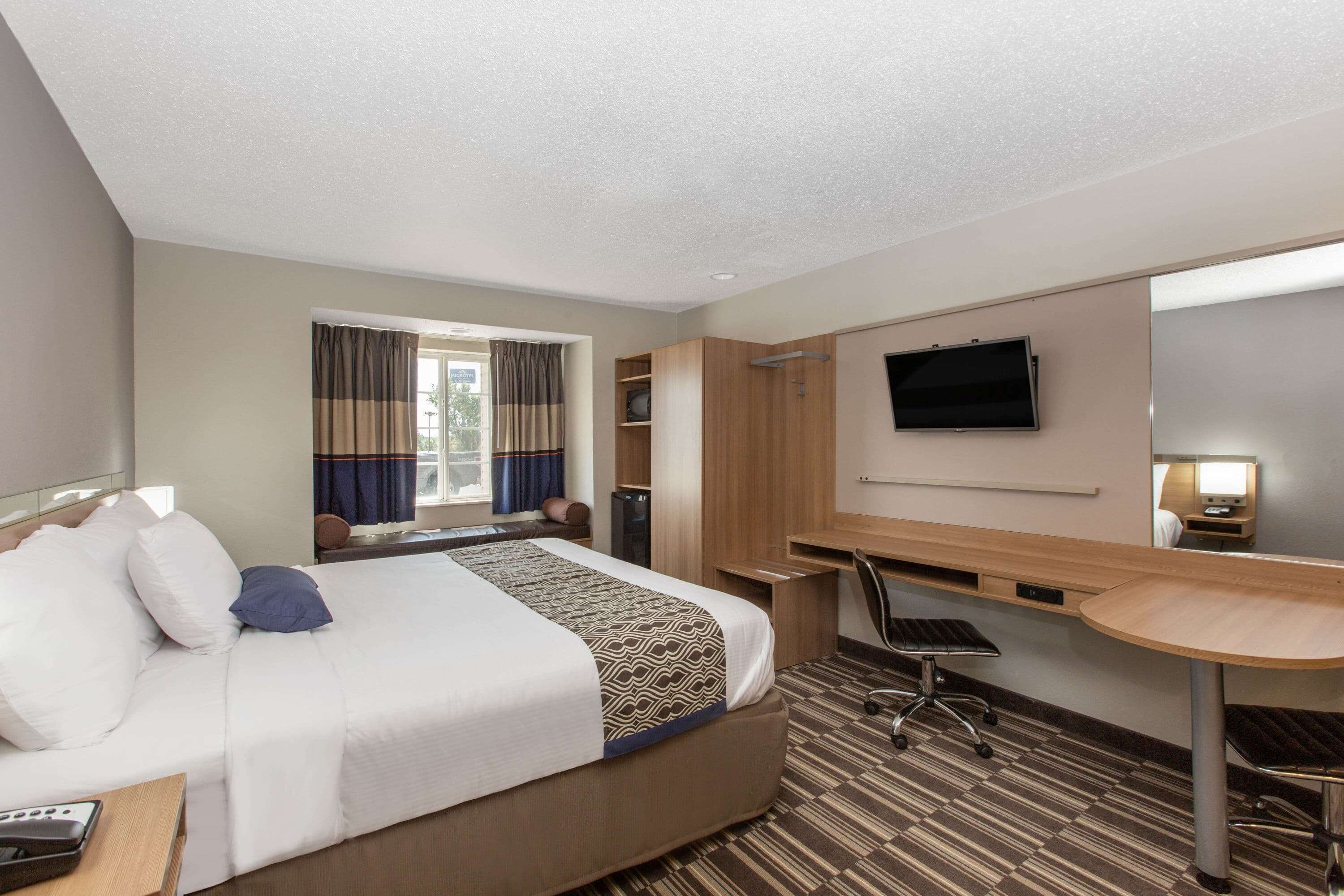 Habitación de hotel con una cama grande, un escritorio, una silla, un televisor y una ventana con cortinas.