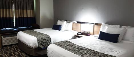 Et hotelværelse med to senge, et vindue med gardiner, et natbord med telefon og vækkeur samt et gulvtæppe med et mønster.