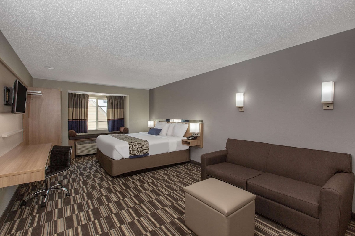 A hotel room with a bed, a desk, a chair, a sofa, and a TV.